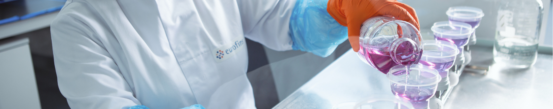 Una técnica de laboratorio con bata, guantes y gafas protectoras, realizando análisis de medios de cultivo y bioindicadores en un laboratorio de Eurofins BioPharma Product Testing. La técnica evalúa la calidad y efectividad de los medios de cultivo utilizados para el crecimiento de microorganismos, asegurando la fiabilidad de los bioindicadores en las pruebas microbiológicas y el control de calidad de productos farmacéuticos.