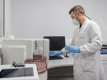 Un técnico de laboratorio con bata, guantes, mascarilla y gafas protectoras, realizando análisis en un laboratorio especializado en el control de agua de grado farmacéutico. El técnico lleva a cabo pruebas rigurosas para garantizar que el agua cumpla con los estándares más altos de pureza y calidad, esenciales para la fabricación de productos farmacéuticos seguros y efectivos.