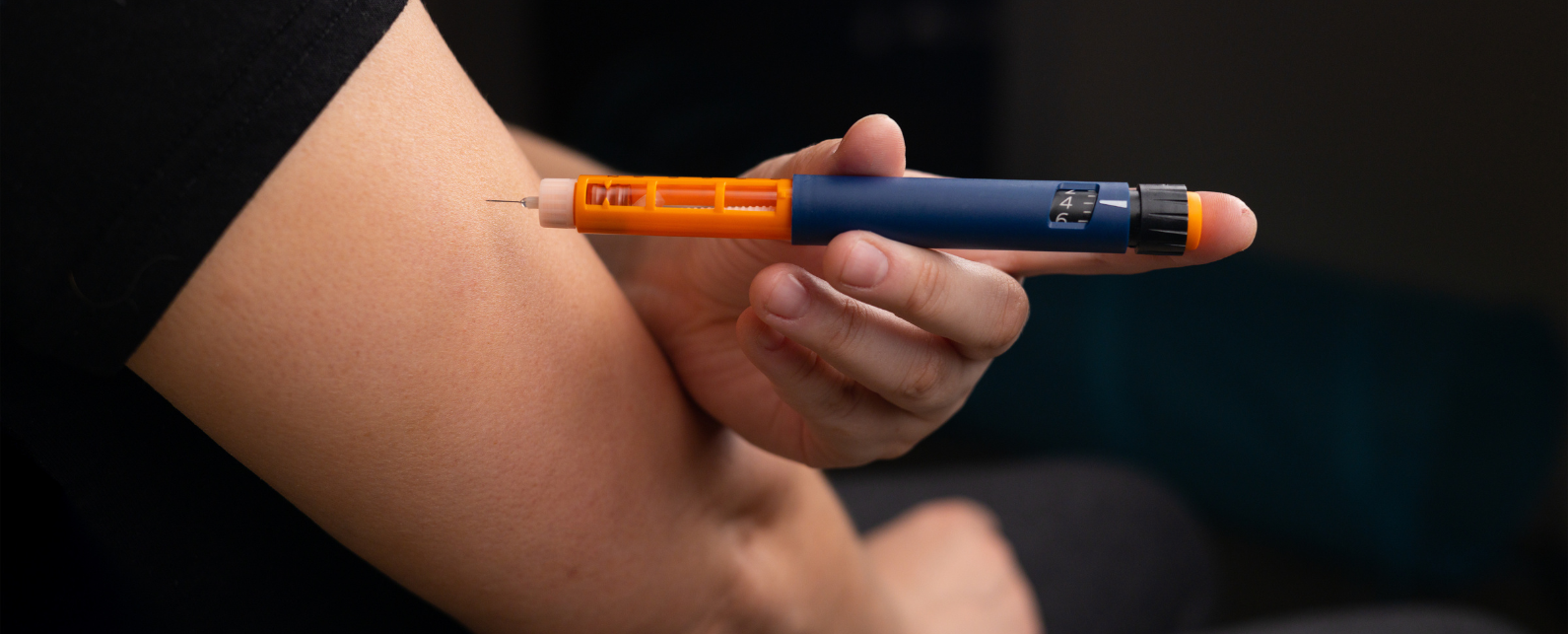 Chairs next to a window to view a lab simulation of a mannequin in a hospital bed with a night stand and IV pole